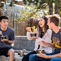 three individuals chatting by a waterfall while eating